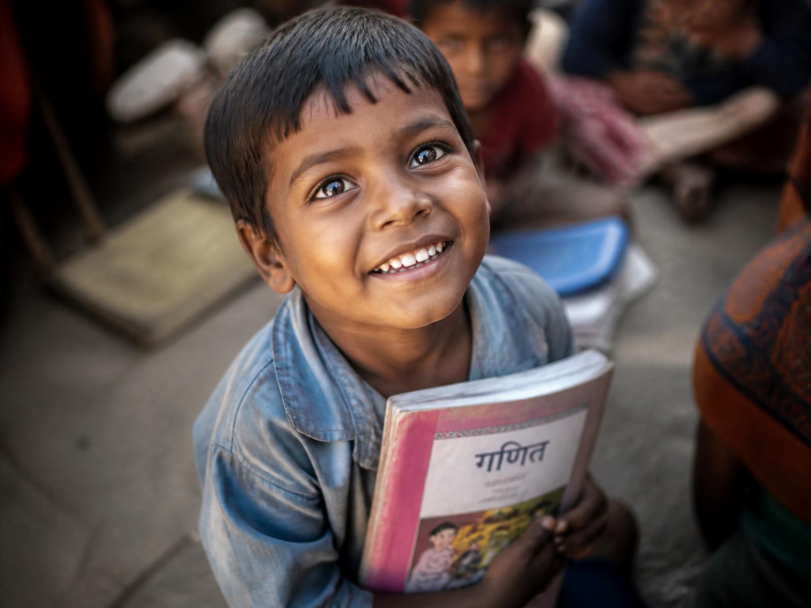 A young child with a school book, looking hopeful